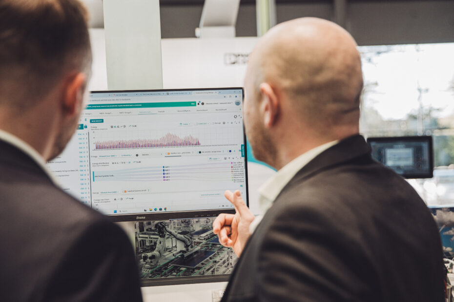 Two professionals viewing the Energy Management Service Cloud dashboard on a monitor, analyzing industrial energy data during a live demonstration.